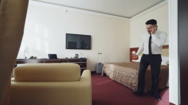 Otel odanın etrafında yürürken cep telefonu üzerinde konuşurken kendinden emin iş adamı. Seyahat, iş ve insan kavramı