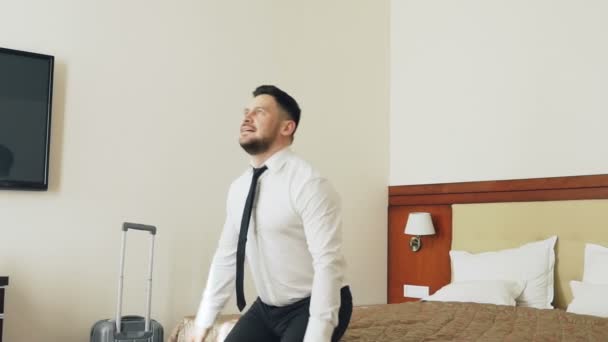 Movimiento lento de feliz hombre de negocios saltando en la cama en la habitación del hotel y acostado relajado sonriendo. Concepto de negocios, viajes y personas — Vídeo de stock