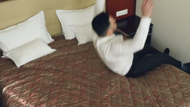 Top view slow motion of happy businessman jumping on bed at hotel room and lying relaxed smiling. Business, travel and people concept — Stock Video