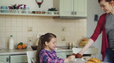 Genç anne evde kahvaltı için bekleyen mutfakta masada oturan kızına şirin lezzetli kek getiriyor