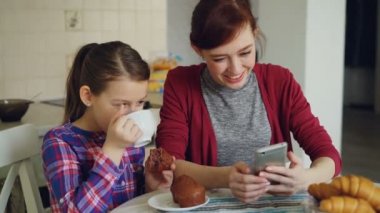 Neşeli anne ve smartphone birlikte tarama ve sabahları kahvaltı sırasında evde mutfak gülümseyen şirin kızı