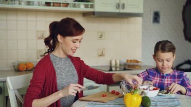 Mutlu genç anne ve neşeli kız yemek mutfakta birlikte evde salata sebze kesme ve konuşuyor. Aile, aşçı ve insanlar kavramı