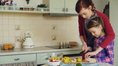 Genç anne sebze düzgün kesmek için sevimli kızı öğretim çok. Küçük kız ile birlikte modern kithcen sevgi dolu anne evde pişirme