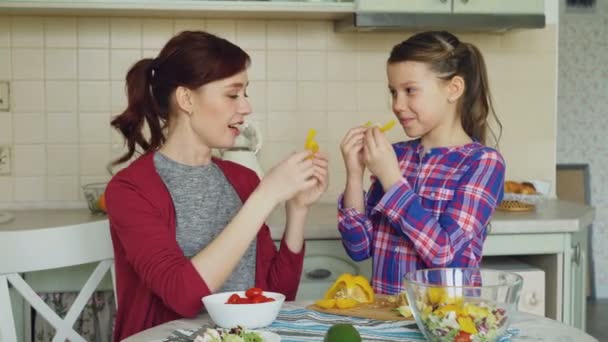 Glada mor och söt glad dotter ha roligt grimaserande fånigt med grönsaker medan matlagning i köket hemma. Familj, cook och människor-konceptet — Stockvideo