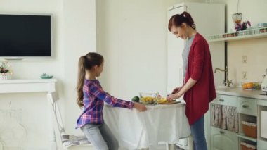 Neşeli anne ve sevimli kızı neşeyle modern mutfakta konuşuyor. Anne kız geldiğinde yemek. Aile, gıda, ev ve insan kavramı