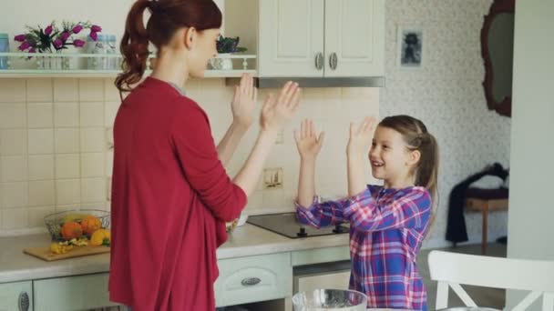 Madre feliz y linda hija divertida jugando aplaudiendo juego de manos y divertirse mientras se cocina en la cocina en casa. Familia, cocina y concepto de personas — Vídeos de Stock