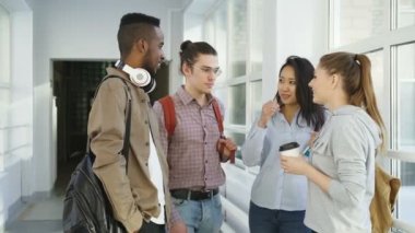 Çok etnik gruptan oluşan grup dört öğrencinin üniversitede Dinkleyen kahve gülüyor olumlu şekilde gülümseyen karıncalar, Birbirinizle konuşmak geniş lighty camsı salonda ayakta
