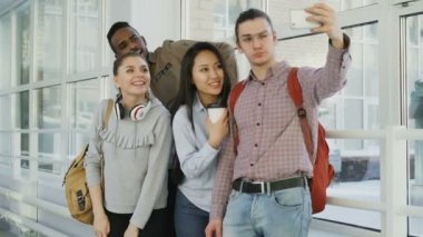Grup çok etnik gruptan oluşan öğrenci üniversite koridorda duran smartphone makinesinde selfie alarak. Telefon ve arkadaşları olumlu poz hipster adam