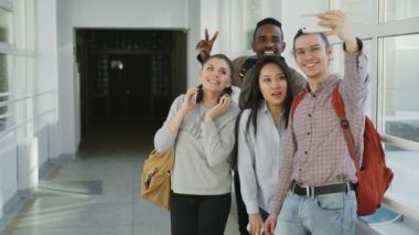 Grup çok etnik gruptan oluşan öğrenci üniversite koridorda duran smartphone makinesinde selfie alarak. Telefon ve arkadaşları olumlu poz hipster adam