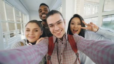 Bakış açısı ile akıllı telefon tutarak ve üniversite koridorunda duran eğleniyor selfie Fotoğraflar konuşan dört olumlu neşeli çekici çok etnik gruptan oluşan arkadaşlar