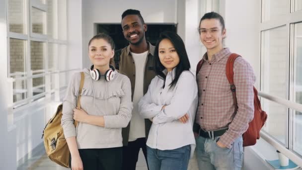 Portret van vier positieve aantrekkelijke multi-etnische mannelijke en vrouwelijke studenten permanent in ruime witte gang in Universiteit kijken camera glimlachen — Stockvideo