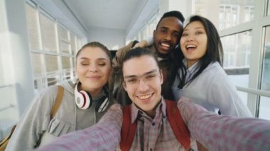 Bakış açısı ile akıllı telefon tutarak ve üniversite koridorunda duran eğleniyor selfie Fotoğraflar konuşan arkadaşlar olumlu etnik grup