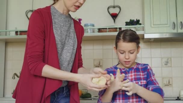 Madre feliz y linda hija cocinar juntos y divertirse revolviendo masa en las manos en la cocina. Concepto de familia, comida, hogar y gente — Vídeos de Stock