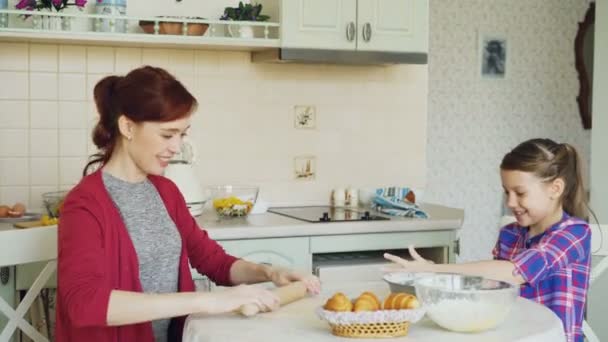 Mãe feliz e filha bonito cozinhar juntos falando na cozinha em casa no fim de semana. Menina batendo palmas com farinha e rindo — Vídeo de Stock