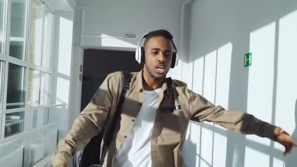 Cool chico afroamericano feliz bailando escuchando música en los auriculares caminando y pasando por el grupo de compañeros de clase haciendo pulgares hacia él — Vídeos de Stock