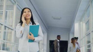 Telefon gülümseyen üniversite koridorunda ile arkadaşları olumlu ayakta konuşurken Asya etnik köken, genç güzel kadın öğrenci portresi