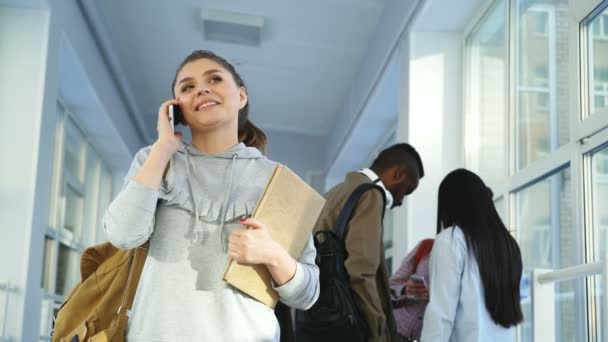 Portré, fiatal, gyönyörű diáklány alkalmi ruhában, beszél telefonon pozitív módon, míg ő groupmates mögött neki valamit megvitatni a — Stock videók