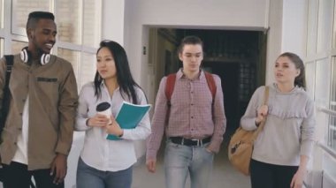 Farklı etnik yapı, dört grup gülümseyen ve gülüyor ve Birbirinizle konuşmak Üniversitesi'nde uzun geniş geniş cam gibi koridorda yürüyor