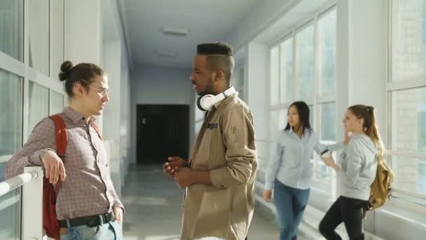 Grupo multi-étnico de estudantes conversando no corredor da universidade tendo pausa. Na vista frontal caras estão conversando uns com os outros na visão traseira meninas estão de pé — Vídeo de Stock