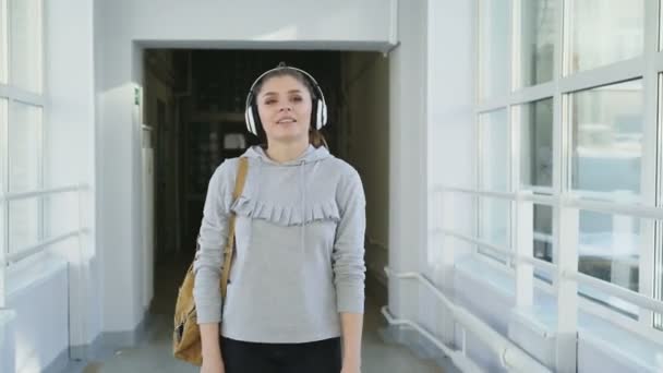 Hermosa estudiante atractiva con auriculares va por el pasillo encontrándose con sus compañeros de grupo dando cinco a su amigo y seguir adelante. Ella muestra el dedo medio al chico afroamericano — Vídeos de Stock