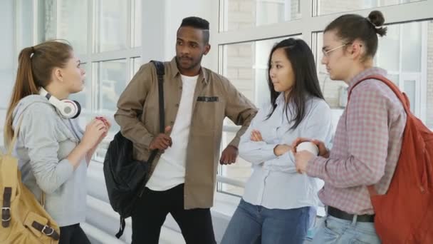 Dolly filmou vista de grupo multi-étnico de estudantes que estão juntos no corredor da faculdade. Menina caucasiana bonita está de pé na frente deles explicando e gesticulando — Vídeo de Stock