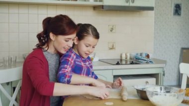 Anne ile birlikte modern mutfak evde otururken ekmek formları kullanarak kurabiye yapma şirin kız gülümsüyor. Aile, gıda ve insanlar kavramı