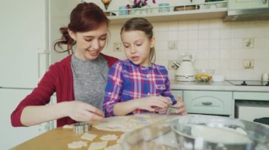 Neşeli anne ile konuşmak ve birlikte modern mutfak evde otururken hamur kırpma ekmek formları kullanarak kurabiye yapma küçük şirin kız. Aile, gıda ve insanlar kavramı