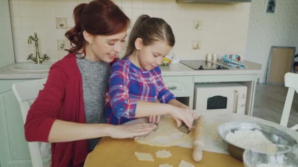 Весела мати і маленька донька роблять печиво разом, використовуючи хлібобулочні форми, обрізаючи тісто, сидячи на сучасній кухні вдома. Концепція сім'ї, їжі та людей — стокове відео