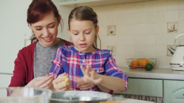 Fröhliche Mutter im Gespräch mit süßer Tochter, die am Wochenende in der Küche Teig mixt und rollt. Familien-, Lebensmittel-, Wohn- und Personenkonzept — Stockvideo