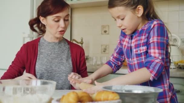 Alegre madre y linda hija rodando masa mientras cocina en la cocina el fin de semana. Concepto de familia, comida, hogar y gente — Vídeos de Stock