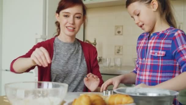 Vrolijke moeder en schattige dochter deeg rollen tijdens het koken in de keuken op weekend. Familie, voedsel, huis en mensen concept — Stockvideo