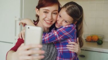 Gülümseyen anne genç komik oynak kızım yapma selfie fotoğraf smartphone kamera evde mutfak ile birlikte. Aile, aşçı ve insanlar kavramı