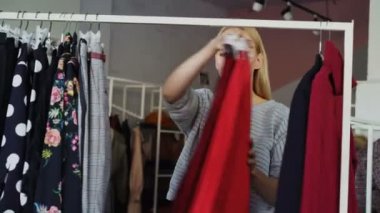 Çekici sarışın kadın moda giyim üzerine raylar, onları bir kenara hareket hızla kontrol ettikten sonra bakıyor. O alışveriş ve gülümseyen keyif alıyor.