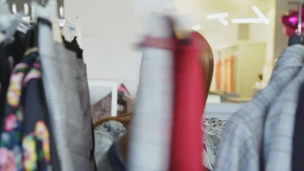 Close-up shot of female student shopping for clothes, looking through colourful garments on hangers, touching and moving them. Womens clothing in the foreground. — Stock Video