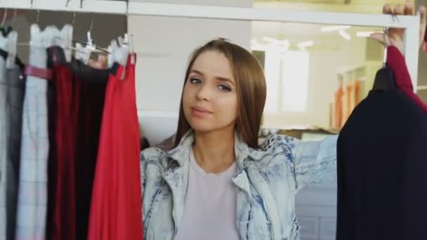 Close-up of young lady shopping for clothes, going through colourful garments on rails, touching and moving them. Trendy womens clothing in the foreground. — Stock Video