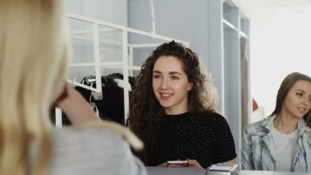 Close-up shot van vrouwelijke klanten betalen voor kleding op kassiers Bureau in kleding boetiek. Jonge vrouw maakt betalen met de slimme telefoon, nemen tas met aankopen en uitgaan — Stockvideo