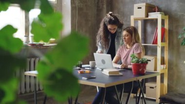 Küçük işletme sahipleri genç modern loft tarzı ofis içinde laptop ile çalışıyoruz. Sarışın oturuyor ve yazarak, esmer ayakta ve fikirler öne.