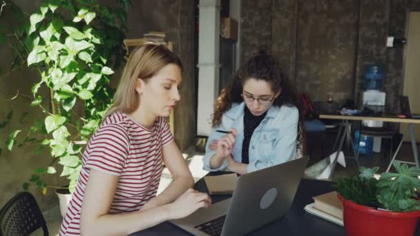 Ambitieuze ondernemers ontwikkelen bedrijfsstrategie zitten in moderne loft stijl kantoor en praten. Een van hen is werken met een laptop, is andere schrijven in notitieblok. — Stockvideo