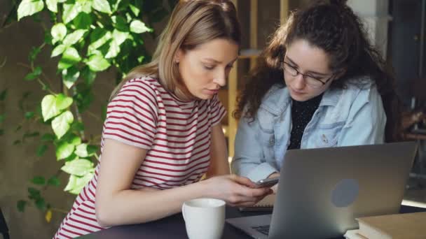 Primer plano de dos alumnas usando un teléfono inteligente. Chica rubia atractiva está tocando la pantalla y charlando con su amigo. Tecnología moderna para los jóvenes concepto . — Vídeos de Stock