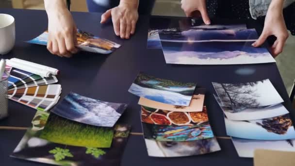 Tilt-up shot van womens handen plaatsen van foto's op tafel in het moderne kantoor. Vrouwelijke ontwerpers zijn foto's van kleur en beeld groeperen en bespreken van illustraties. — Stockvideo