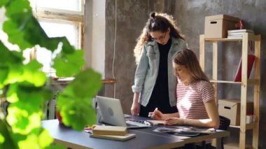 İki çekici arkadaşları tasarım notları defter, laptop perde ve tablo fotoğrafları izlerken görüşüyorlar. Kadınlar konuşmaya ve duygusal el hareketi.