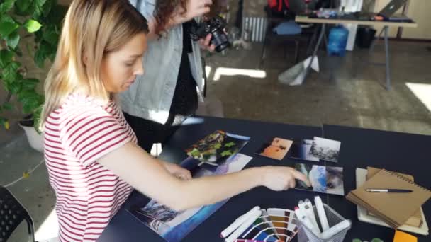 Collèges créatifs placer des photos sur la table et tirer à plat laïc tout en parlant de la conception de projet. Vue du dessus de la table moderne avec illustrations . — Video