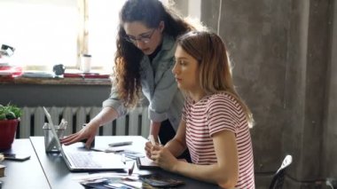 Genç tasarımcı onun meslektaşım onun laptop perde gösterilirken not defterinde görüntüleri çizim ve fikir paylaşımı. Kadın tablo fotoğrafları izlerken ve renk paleti kontrol.