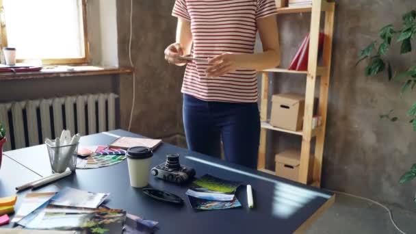 Tilt-up shot of young travel blogger making pictures of her desk with smart phone. Ella está moviendo diferentes cosas en su mesa y disparando . — Vídeos de Stock