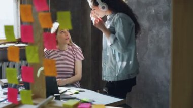 Onun iş arkadaşı office girerken kadın Tasarımcısı laptop ile çalışıyor. Misic için sonra kulaklık ve onun iş arkadaşı yardım başlangıç alarak dinlediğini.