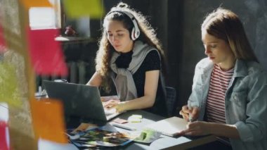 Yaratıcı tasarımcılar ekibi birlikte hafif ofisinde çalışıyor. Esmer Bayan müzik ve laptop ile çalışma ve sarışın bir kadın Not Defteri'nde görüntüler çekiyor