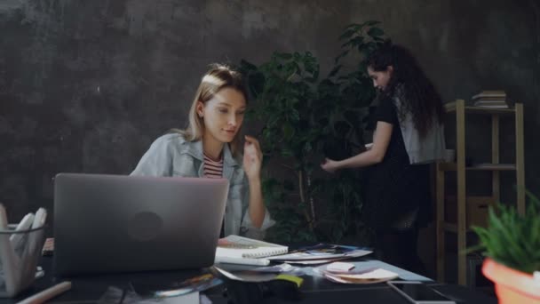 若い創造的なデザイナーが図面と彼女の同僚を噴霧し、大規模な緑の植物を洗浄しながらメモ帳開発プロジェクトでの記述。友好的な協力の概念. — ストック動画