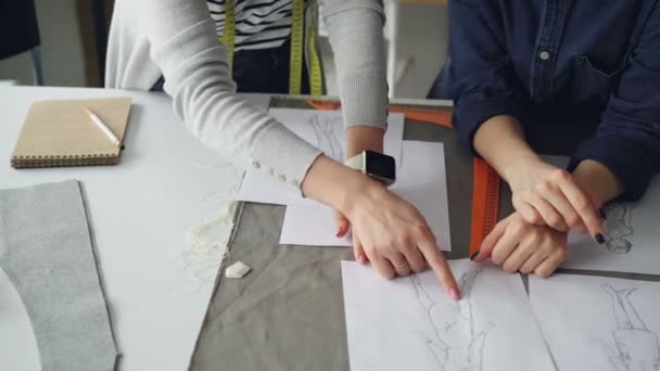 Un primo piano di mani di sarti che esaminano schizzi sulla scrivania da cucito. Le donne stanno discutendo di abbigliamento. Creativi sarti concetto di lavoro . — Video Stock