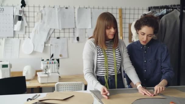 Team van creatieve ontwerpers werkt met kleding patronen en stof in kleermakers winkel. Jonge vrouwen zijn geconcentreerd op het meten. Naaien items en tools in de achtergrond. — Stockvideo