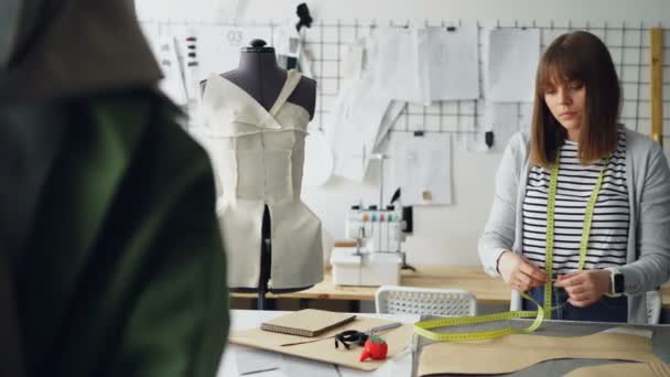 Ελκυστική γυναίκα ράφτης μέτρηση ενδυμασία μοντέλα με μεζούρα στο μαγαζί της φως ράφτες. Καθημερινές εργασίες στην κατασκευή βιομηχανίας έννοια ρούχα. — Αρχείο Βίντεο